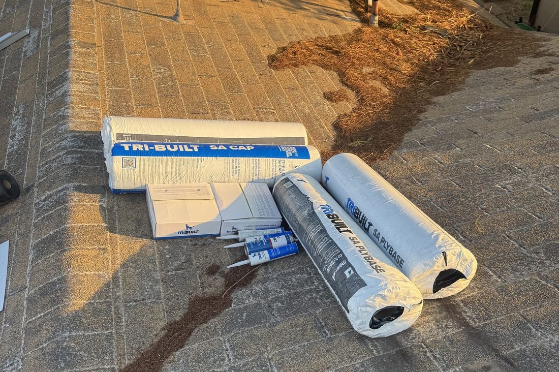 Low-slope commercial roof in Phoenix with self-adhered modified bitumen base sheet and cap sheet rolls staged beside a rooftop HVAC unit